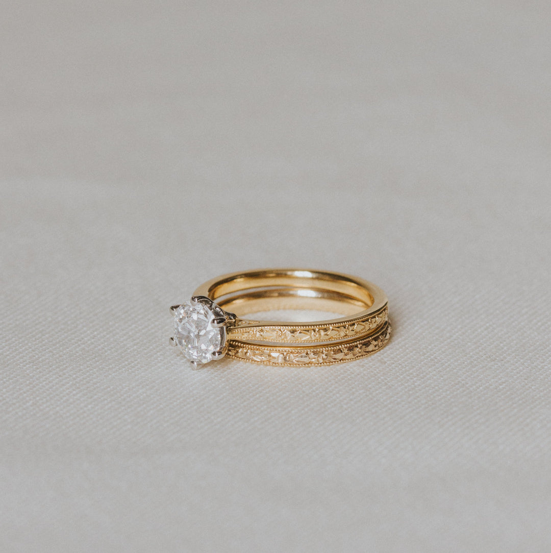 Gold engraved ring with a diamond on a light gray background